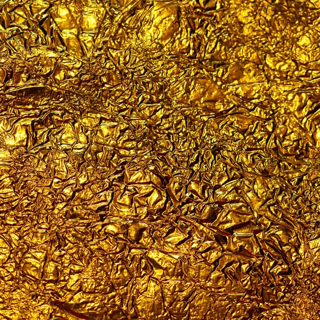 Superficie de pan de oro con pliegues y arrugas finas que reflejan la luz de forma irregular